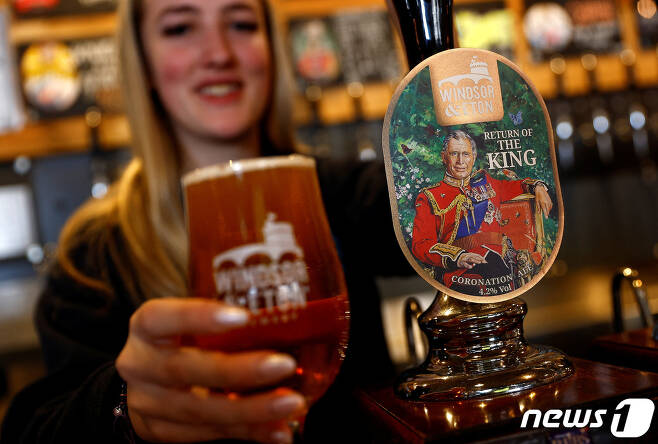 5일(현지시간) 영국 런던 근교 윈저의 한 맥주집에서 한 여성 종업원이 찰스 3세 국왕의 대관식을 기념하기 위한 맥주와 잔을 들고 있다. 2023.4.5 ⓒ 로이터=뉴스1 ⓒ News1 정윤미 기자