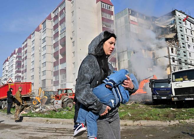 28일(현지시각) 우크라이나 키이우에서 아이를 안은 한 여성이 러시아 공습으로 파괴된 아파트 건물을 지나가고 있다. /AFP 연합뉴스