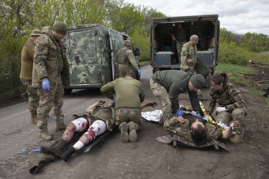 지난 11일(현지시간) 우크라이나 동부 격전지 바흐무트 인근의 한 도로에서 전투 중 부상을 입은 우크라이나 군인들이 군의료진에게 응급처치를 받고 있다. AP 연합뉴스