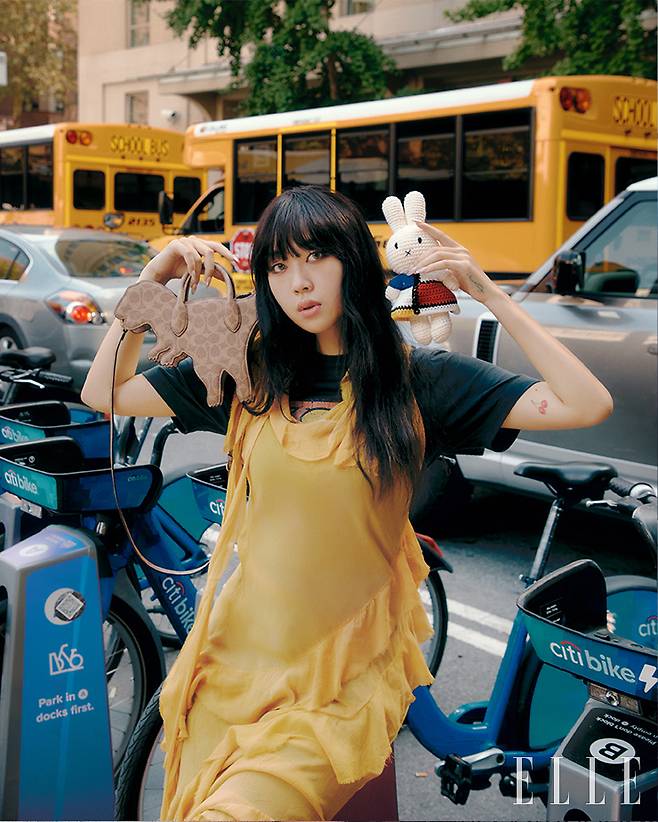 공룡 모티프의 시그니처 캔버스 렉시 백과 시폰 소재의 옐로 드레스와 매치한 티셔츠 모두 Coach.