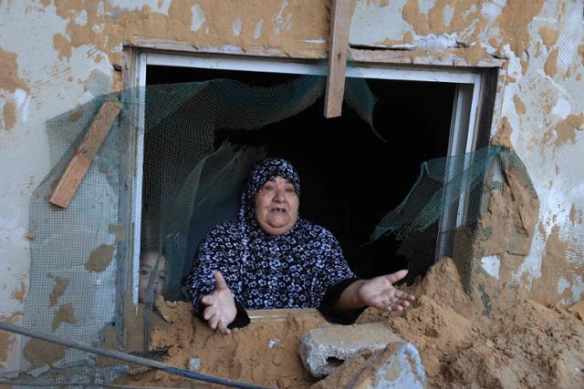 15일 이스라엘군의 공습으로 파괴된 가자지구 내 한 난민촌 건물 안에서 한 여성이 황망한 듯 두 손을 들어 보이고 있다. 가자=AFP 연합뉴스