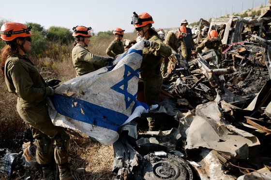 1일(현지시간) 이스라엘 군인들이 남부 네티보트 근처 가자 지구에서 하마스 무장괴한들의 공격을 받아 파괴된 차량에서 유해와 이스라엘 국기를 수습하고 있다. 로이터=연합뉴스