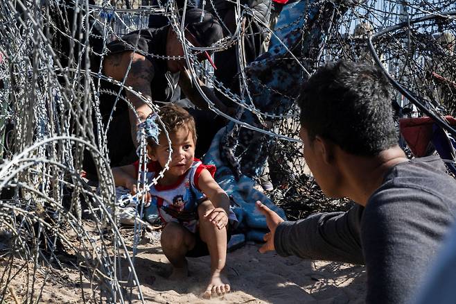 2024년 3월 22일 멕시코에서 미국 텍사스주 엘패소로 넘어가는 이민자들 사이에서 한 어린 소년이 국경 철조망을 통해 기어가고 있다. / 로이터 연합뉴스