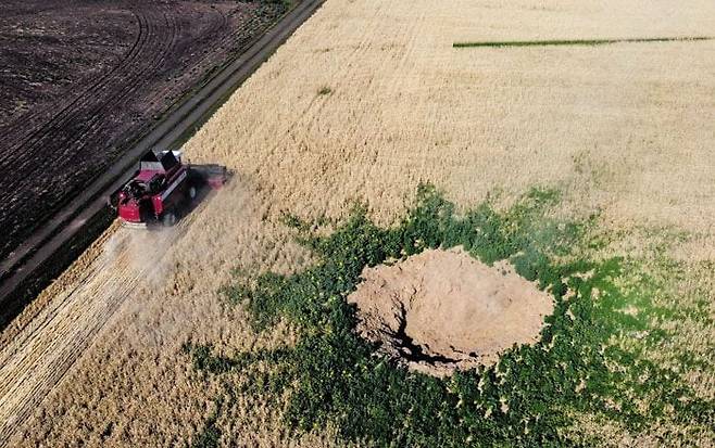 2022년 우크라이나 동부 도네츠크주 크라마토르스크에서 한 농민이 러시아군의 공습을 받아 구덩이가 움푹 파인 밀밭 옆을 지나며 콤바인으로 밀을 수확하던 모습./AFP 연합뉴스