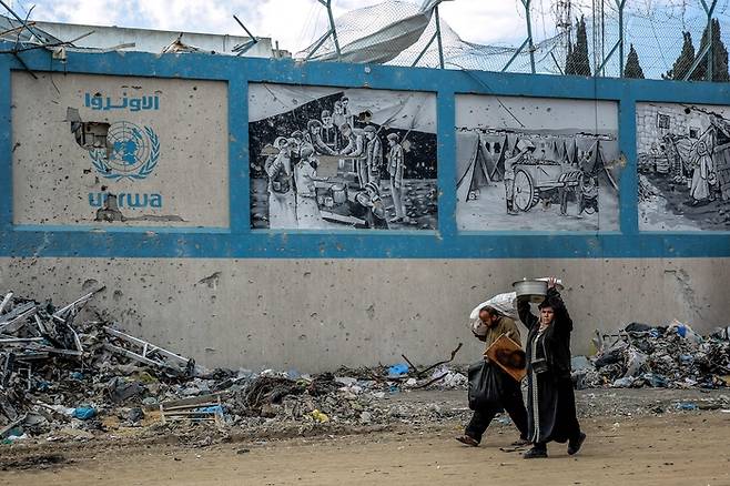 지난 2월15일(현지시간) 가자지구 북부 가자시티에서 팔레스타인 피란민들이 이스라엘군의 폭격을 받은 유엔 팔레스타인 난민구호기구(UNRWA) 본부를 지나고 있다. AFP연합뉴스