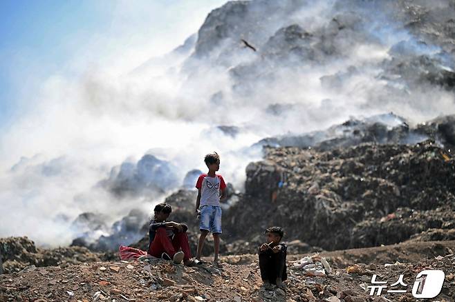 인도 어린이들이 22일 뉴델리 가지푸르 쓰레기 매립장에서 불타는 쓰레기로부터 피어오르는 연기를 배경 삼아 앉아있다. 2024.04.22 ⓒ AFP=뉴스1 ⓒ News1 김성식기자