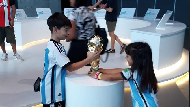 지난달 23일(현지 시각) 아르헨티나 로사리오의 산타페 스포츠 박물관에 아르헨티나 축구 국가대표팀 유니폼을 입고 방문한 어린이들이 FIFA 월드컵 트로피 레플리카를 만져보고 있다. /서유근 특파원