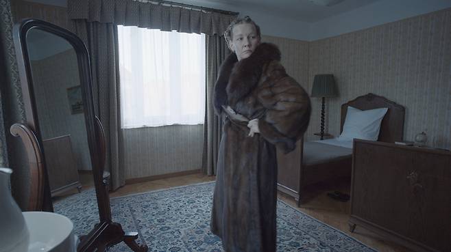 아내 헤트비히(산드라 휠러)는 아름답게 꾸민 집에 자부심을 가지고 있다. 그는 전쟁 중에도 립스틱이나 모피코트 같은 값비싼 물건을 구해 자신을 꾸민다. 찬란 제공