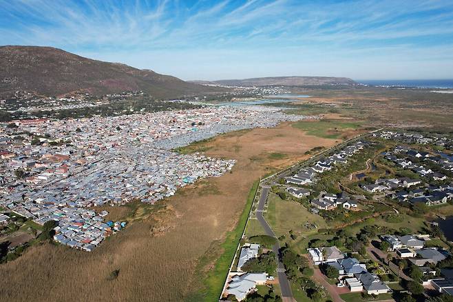 남아프리카공화국 케이프타운 외곽 미셸호수 인근의 마시푸멜렐레 지역을 무인항공기에서 찍은 장면. 흑인이 거주하는 판자촌이 밀집한 왼쪽과 부유한 백인이 거주하는 전원주택 단지가 극명한 대조를 이룬다. REUTERS
