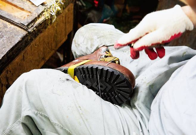 장인이 두꺼운 등산화를 다리 사이에 끼고 바느질하고 있다.