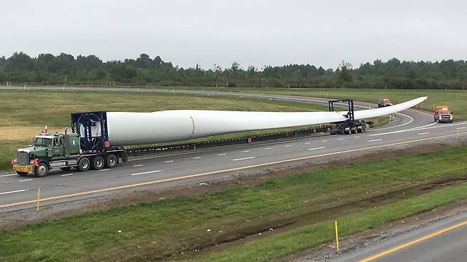 미국 뉴욕주의 한 도로에서 풍력 발전기의 바람개비를 이루는 ‘블레이드’ 1개가 화물차에 실려 옮겨지고 있다. 일반적인 풍력 발전기는 블레이드 3개로 이뤄진다. 블레이드는 길이가 최대 100m에 달하기 때문에 도로를 통해 이송하기가 어렵다. 미국 뉴욕주 교통국 제공