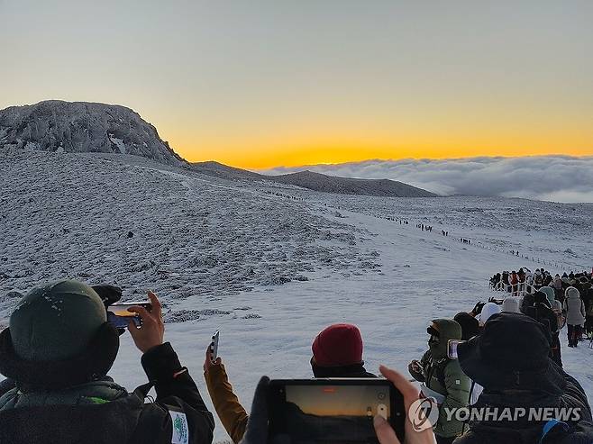 갑진년 첫날 한라산 해돋이 등반객 (제주=연합뉴스) 고성식 기자 = 새해 첫날 한라산 백록담이 보이는 윗세오름에서 제주도민과 관광객들이 구름 위로 솟아오른 해를 보며 사진을 찍고 새해 소망을 빌고 있다. 2024.1.1 koss@yna.co.kr