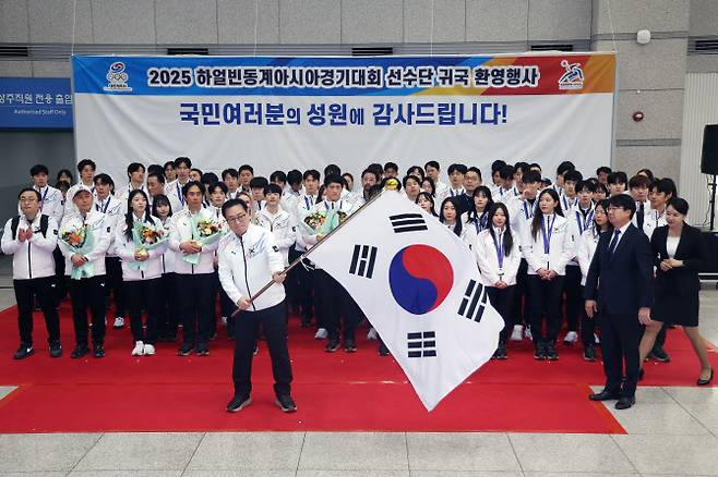 최홍훈 하얼빈 동계아시안게임 선수단장이 15일 인천공항 제1터미널에서 열린 2025 하얼빈 동계아시안게임 귀국 환영행사에서 윤성욱 대한체육회 사무총장에게 단기를 반납하기 전 흔들고 있다. 사진=연합뉴스
