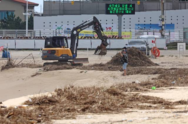 강원 강릉시 안목해변에서 굴착기가 폭우와 너울성 파도로 쓰레기가 쌓인 해변을 청소하고 있다. 연합뉴스
