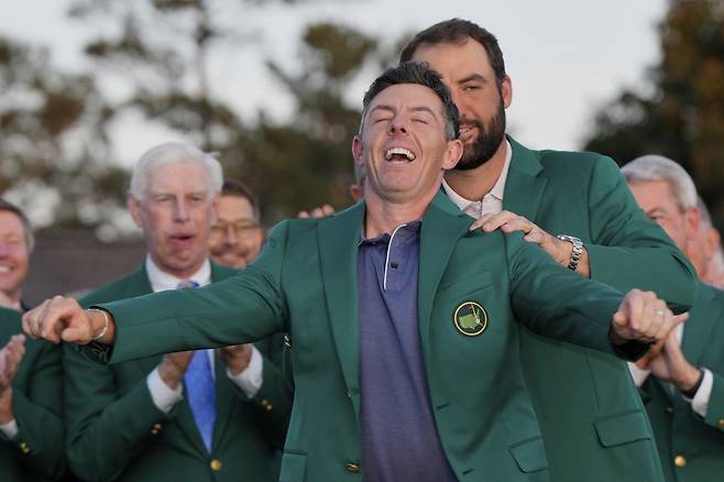 로리 매킬로이(북아일랜드)가 13일(현지 시간) 미 조지아주 오거스타 내셔널 골프클럽에서 열린 제89회 마스터스 토너먼트 정상에 올라 지난해 우승자 스코티 셰플러(미국)가 입혀 주는 ‘그린 재킷’을 입고 있다. 매킬로이는 최종 합계 11언더파 277타로 저스틴 로즈(영국)와 동타를 이뤄 연장 끝에 우승, 커리어 ‘그랜드 슬램’을 달성했다. 오거스타(미국) ㅣAP 뉴시스