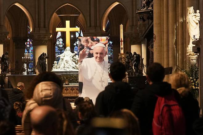 21일 교황청이 프란치스코 교황의 선종을 공식 발표한 뒤, 파리 노트르담 대성당 내부에 설치된 프란치스코 교황의 사진 앞에서 사람들이 기도하고 있다. /AP 연합뉴스