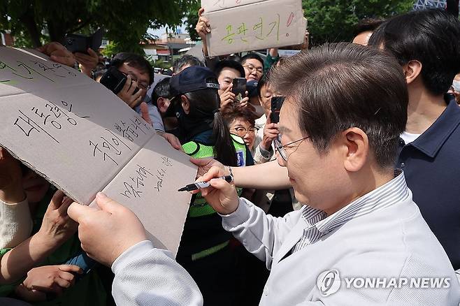 공판 연기 환영 팻말에 이재명 후보 '맞습니다' (전주=연합뉴스) 류영석 기자 = 더불어민주당 이재명 대선 후보가 '골목골목 경청투어:국토종주편'에 나선 7일 전북 전주시 풍남문 앞 광장에서 지지자들에게 인사를 하던 도중 한 지지자가 든 '공판 연기 환영, 대통령은 국민이 뽑습니다'라는 팻말에 사인을 하고 있다.
이날 서울고등법원은 오는 15일 예정됐던 이 후보의 공직선거법 위반 혐의 사건 파기환송심 첫 공판을 오는 6월 18일로 연기했다. 2025.5.7 ondol@yna.co.kr