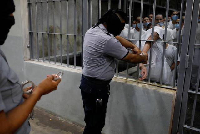 지난달 4일 엘살바도르 테콜루카의 테러범수용센터(CECOT) 교도소에서 교도관이 수감자에게 수갑을 채우고 있다. 엘살바도르 등으로 이민자를 추방하고 있는 도널드 트럼프 미국 행정부는 추방자 수용국 확대를 추진 중이다. 테콜루카=로이터 연합뉴스