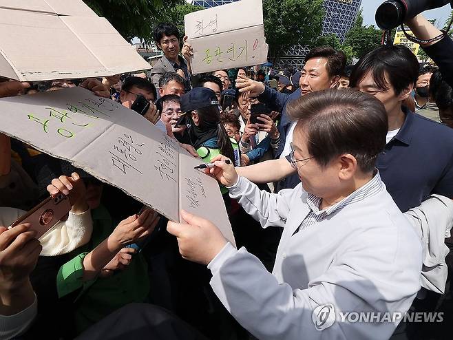 공판 연기 환영 팻말에 이재명 후보 '맞습니다' (전주=연합뉴스) 류영석 기자 = 더불어민주당 이재명 대선 후보가 '골목골목 경청투어:국토종주편'에 나선 7일 전북 전주시 풍남문 앞 광장에서 지지자들에게 인사를 하던 도중 한 지지자가 든 '공판 연기 환영, 대통령은 국민이 뽑습니다'라는 팻말에 사인을 하고 있다.
이날 서울고등법원은 오는 15일 예정됐던 이 후보의 공직선거법 위반 혐의 사건 파기환송심 첫 공판을 오는 6월 18일로 연기했다. 2025.5.7 ondol@yna.co.kr