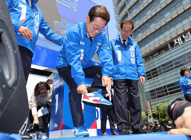 이재명 더불어민주당 대통령 후보가 6·3 대선 공식 선거운동 첫날, 양복과 구두를 벗고 파란색과 빨간색이 섞인 선거운동복과 운동화를 착용하고 유세에 나섰다. 사진은 이재명 더불어민주당 대선후보가 제21대 대통령선거 공식 선거운동이 시작된 12일 오전 서울 청계광장에서 열린 중앙선거대책위원회 출정식에서 운동화를 신고 있는 모습. /사진=공동취재