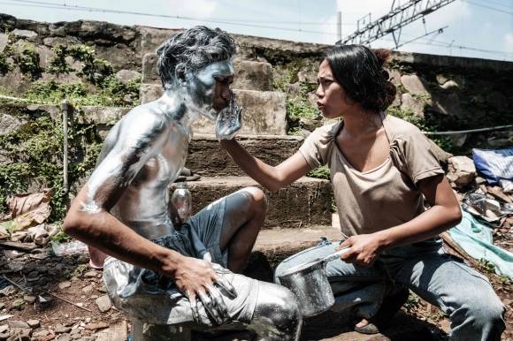 지난달 7일 인도네시아 자카르타에서 아리 무난다르(왼쪽)가 아내의 도움을 받아 몸에 은색 페인트칠을 하고 있다. 무난다르는 온몸에 은색 페인트를 칠한 채 교차로에서 운전자들에게 구걸해 생계를 유지하고 있다. AFP 연합뉴스