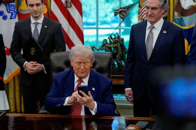 도널드 트럼프 미국 대통령이 23일(현지시간) 백악관 집무실에서 진행한 행정명령 서명식에서 취재진과 질의응답을 하던 중 전화벨이 울리자 애플 아이폰 알림음을 무음으로 설정하고 있다. /로이터=뉴스1
