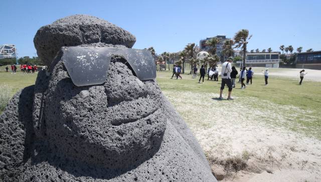 제주시 조천읍 함덕해수욕장에 설치된 선글라스를 낀 돌하르방 뒤로 가벼운 옷차림을 한 관광객들이 이동하고 있다. 뉴스1