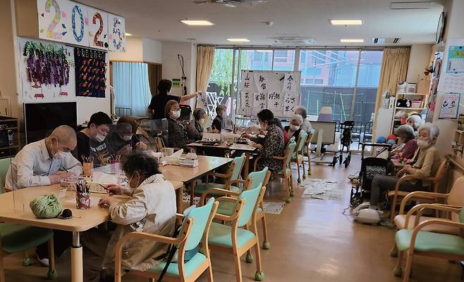 스마일 메종 히키후네 1층 거실에서 붓글씨와 꽃꽂이를 하는 10여 명의 노인./ 최인한
