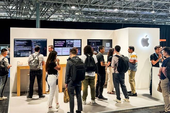 2024년 12월 6일 캐나다 밴쿠버에서 개최된 신경정보처리시스템학회(NeurIPS)에 참여한 미국 IT 기업 애플 부스. NeurIPS는 머신러닝 및 인공지능(AI) 분야에서 가장 큰 연례 학회다. 애플은 자사의 머신러닝 연구를 시연했다. 애플은 AI를 핵심 기술과 기업 전략의 중심에 둔 AI-first(우선)기업이 아님에도 2025년 2월 향후 4년간 AI에 5000억 달러(한화 약 697조 원) 달러를 투자하겠다고 밝혔다. Apple 제공