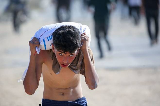 팔레스타인 땅 가자지구 중부 데이르알발라에서 피란민 청년이 세계식량기구(WFP) 창고에서 구한 식량 자루를 어깨에 올려 옮기고 있다. AFP 연합뉴스