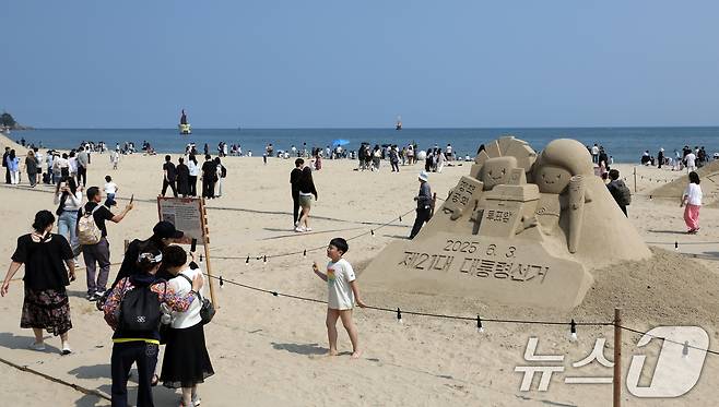 제21대 대통령 선거일이자 초여름 날씨를 보인 3일 오후 부산 해운대해수욕장에 설치된 대통령 선거 홍보 모래작품 뒤로 시민, 관광객 등이 더위를 식히고 있다. 2025.6.3/뉴스1 ⓒ News1 윤일지 기자