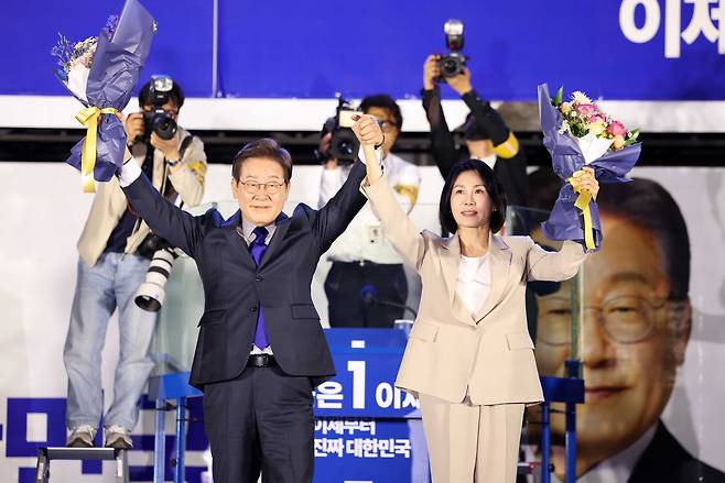 Lee Jae-myung, who is all but certain to be elected president, and his wife Kim Hye-kyung greet supporters with raised arms after receiving bouquets during a public vote-count event hosted by the party near the National Assembly in Yeouido, Seoul, on Wednesday. (Pool Photo via Yonhap)