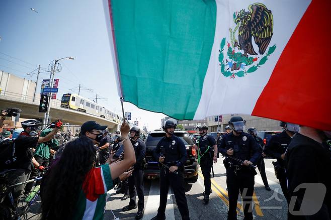 8일(현지시간) (서울=뉴스1) 김지완 기자 = 미국 캘리포니아주 로스앤젤레스(LA)에서 이민 당국의 대규모 불법 이민자 단속에 반대하는 시위대가 경찰 앞에서 멕시코 국기를 흔들고 있다. 2025.06.08 ⓒ 로이터=뉴스1 ⓒ News1 김지완 기자