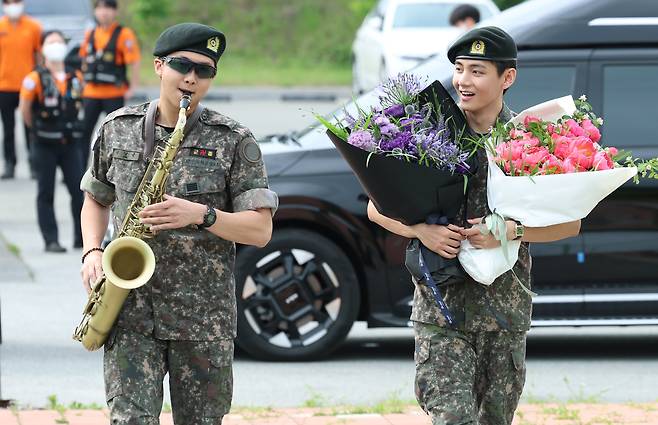 BTS members RM (left) plays the saxophone while V holds bouquets during their discharge ceremony at a soccer field in Chuncheon, Gangwon Province on June 10. /News1