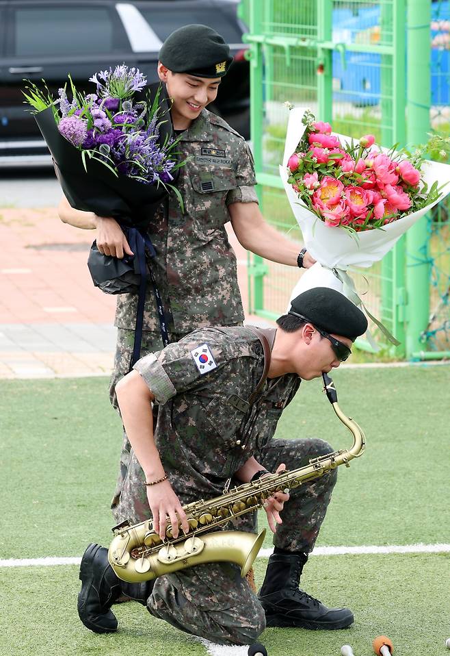 BTS members RM (front) plays the saxophone while V holds bouquets during their discharge ceremony at a soccer field in Chuncheon, Gangwon Province on June 10. /News1