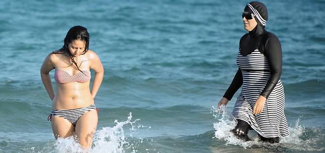 튀니지 북부의 한 해수욕장에서 부르키니(얼굴과 손발을 제외한 전신을 가린 무슬림 여성 수영복)를 입은 여성(오른쪽)과 비키니를 입은 여성(왼쪽)이 물놀이를 즐기고 있다. /AFP 연합뉴스