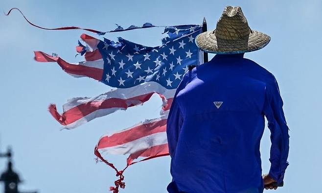 도널드 트럼프 미국 대통령의 79번째 생일이자 미 육군 창설 250주년 기념 열병식이 열린 14일(현지시각) 플로리다 웨스트팜비치에서 열린 ‘노 킹스’ 집회에서 한 시민이 찢어진 성조기를 들고 트럼프 행정부를 규탄하고 있다. 웨스트팜비치/AFP 연합뉴스