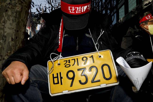 2022년 12월7일 열린 화물연대 결의대회에 참석한 한 조합원이 목에 자신의 차량 번호판을 매단 채 자리에 앉아 있다. 문재원 기자