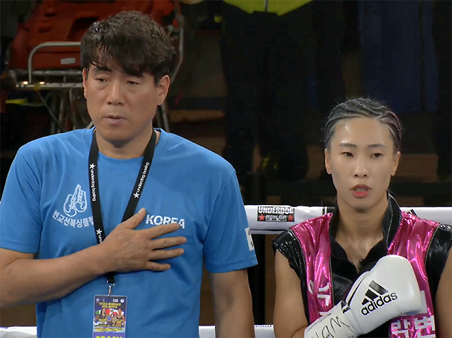 대전변교선복싱클럽 변교선 관장과 박혜수가 2025년 6월 이탈리아 노바라 ‘팔라이고르 고르곤촐라’ 세계복싱협회 여자 플라이급 골드타이틀매치 시작 전 태극기에 경례하며 애국가를 부르고 있다. 사진=이탈리아복싱연맹(Federazione Pugilistica Italiana) 영상 화면