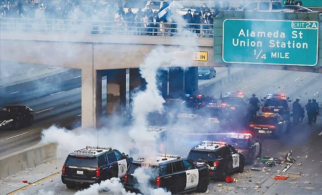 미국 이민세관단속국(ICE)의 불법 이민자 단속·체포에 항의하는 시위대가 8일(현지시간) 캘리포니아주 로스앤젤레스(LA) 도심 101번 고속도로에서 경찰과 대치했다. 시위대 공격으로 일부 경찰차가 파손됐고 도로에 연기가 피어오르고 있다. AFP연합뉴스