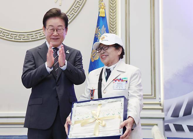 이재명 대통령이 27일 청와대 영빈관에서 열린 ‘호국보훈의 달, 대통령의 초대’ 행사에서 특별 초청 대상자인 6·25전쟁 참전 유공자 이춘자 참전 용사에게 광목 이불 선물을 전달한 뒤 기념촬영을 하고 있다./연합뉴스