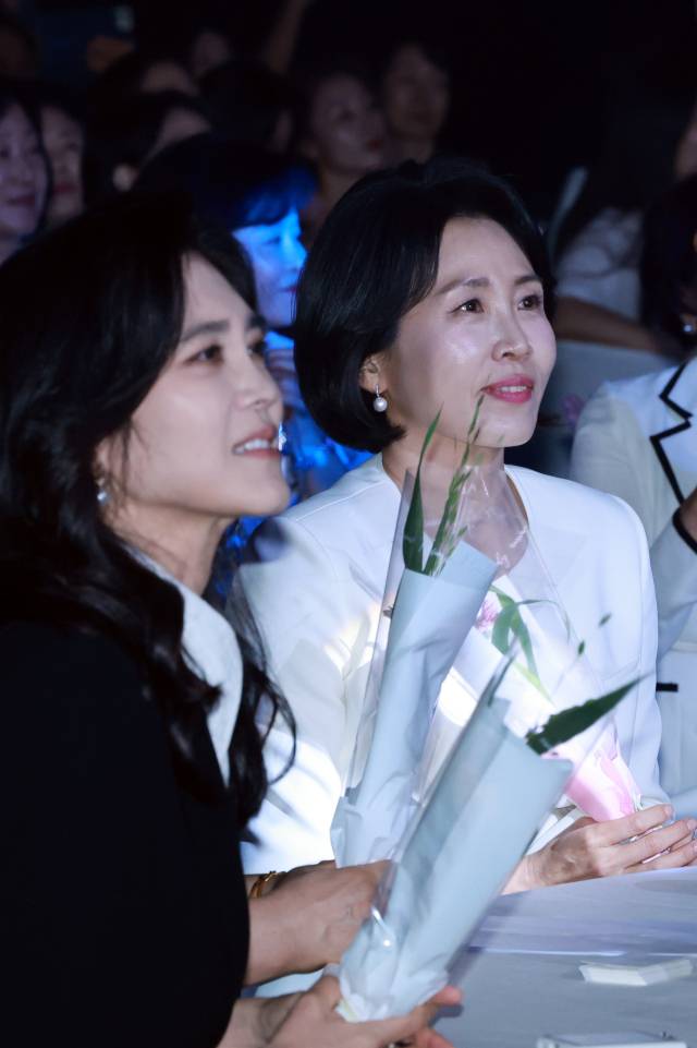 이재명 대통령의 배우자 김혜경 여사가 1일 서울 중구 신라호텔 다이너스티홀에서 열린 제4회 여성기업주간 개막식에 참석해 어린이 합창단원에게 받은 꽃을 들고 축하 공연을 보고 있다. 왼쪽은 이부진 호텔신라 사장. 연합뉴스