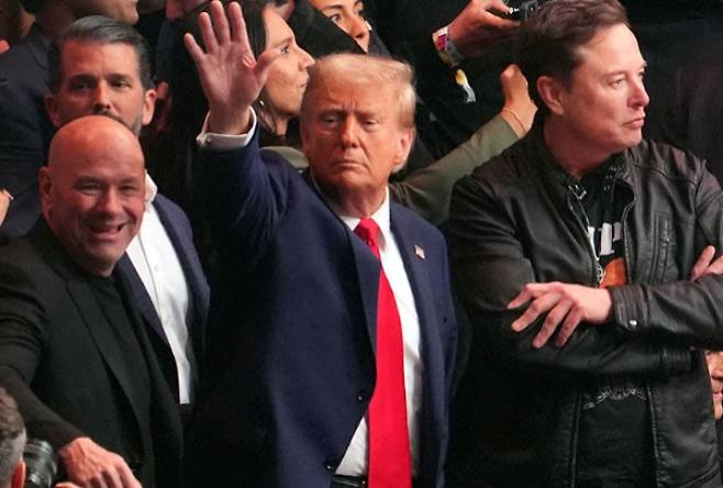 도널드 트럼프 미국 대통령(당시 당선인·사진 가운데)이 지난해 11월 16일(현지시간) 뉴욕 매디슨스퀘어가든에서 열린 UFC 경기장에 입장하면서 관객들을 향해 손을 흔들고 있다. 트럼프 대통령 왼쪽은UFC 데이나 화이트 회장, 오른쪽은 테슬라 일론커스크 최고경영자(CEO). 연합뉴스