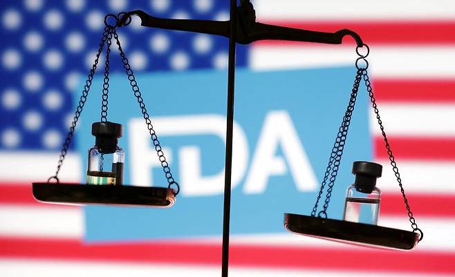 미국 식품의약국(FDA) 로고를 배경으로 저울에 약병(바이알)이 올려져 있다. /REUTERS/Dado