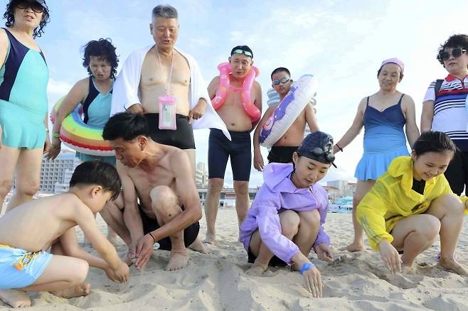 지난 2일 북한 강원도 원산의 원산-갈마 해안관광지구에서 어린이들이 모래사장에 ‘우리 조국’이라고 쓰는 모습을 어른들이 지켜보고 있다. 2025.7.4 원산 AP 뉴시스