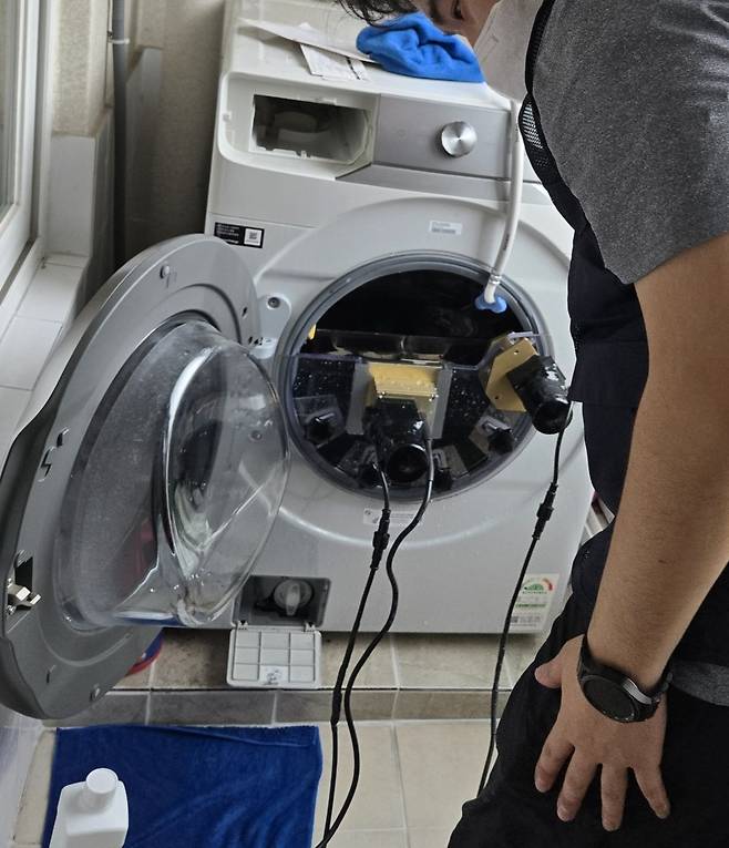 물이 채워진 삼성전자 세탁기에 초음파 발생 기기가 연결돼 있다. 검은색 기기가 세탁기 본체에 진동을 가하면 내부에 고착된 오물이 탈락해 세척이 진행된다. 김지훈 기자.