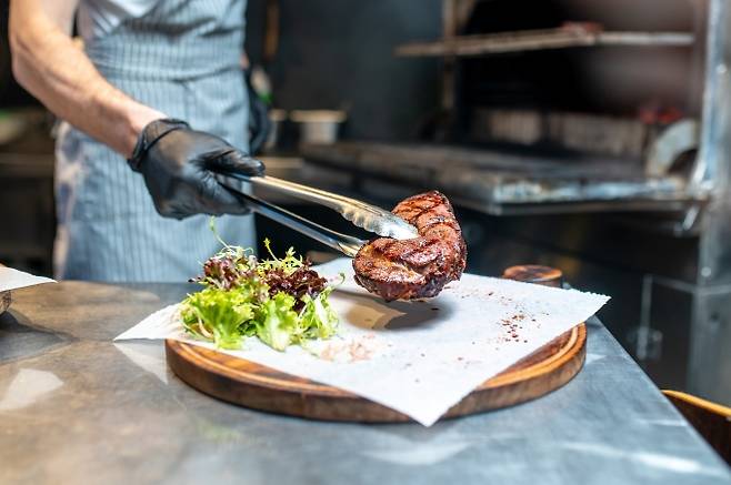 레스토랑 주방에서 스테이크를 내놓고 있는 셰프. 최근 미국에서는 일부 식당이 저가 부위를 접착해 고급 스테이크처럼 판매한 사례가 논란이 되고 있다. 사진=123RF