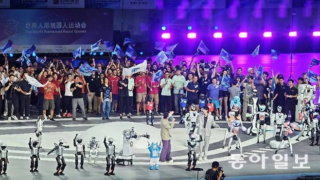 14일 세계휴머노이드로봇대회 개막식에서 로봇과 참가팀 관계자들이 대회 주제가에 맞춰 깃발과 손을 흔들고 있다. 베이징=김철중 특파원 tnf@donga.com