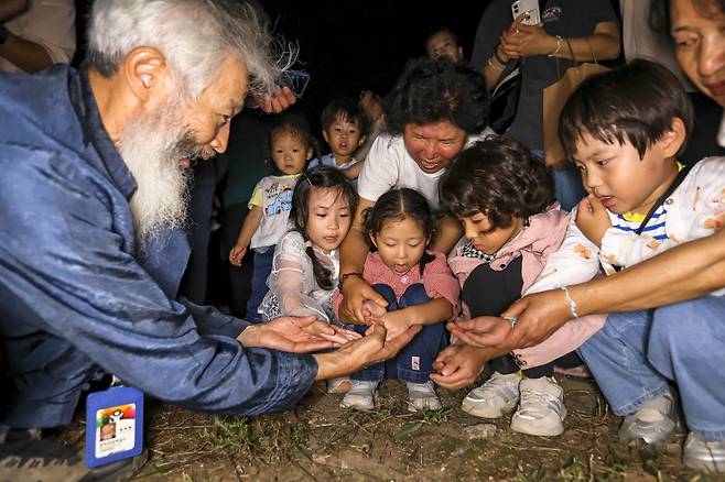 전북 무주군 반딧불축제의 하이라이트인 ‘반딧불이 신비 탐사’에 참여한 어린이들이 해설사의 손에 앉은 반딧불이를 보고 있다. 무주군 제공