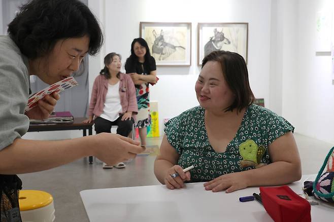 정은혜 작가(오른쪽)가 8월22일 오후 경기 양평군 강상면 어메이징 아웃사이더 아트센터 전시장에서 관람객들에게 사인을 해주자 관람객이 “너무 작품 같은 사인”이라며 감탄하고 있다. 정용일 선임기자 yongil@hani.co.kr